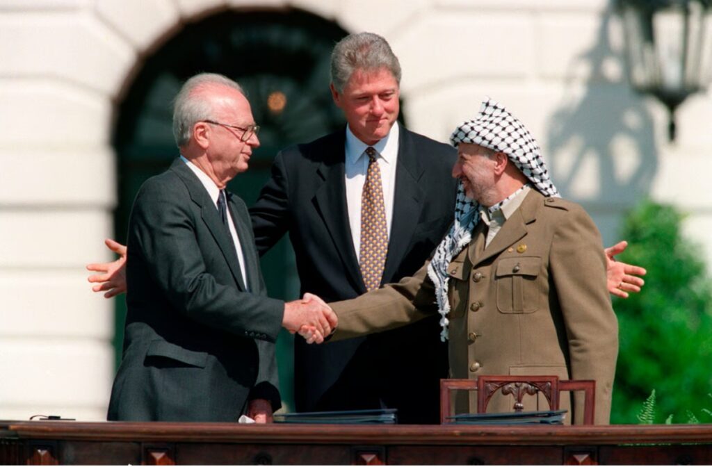 Президент США Билл Клинтон наблюдает, как премьер-министр Израиля Ицхак Рабин и лидер ООП Ясир Арафат обмениваются рукопожатием после подписания Соглашений Осло в Вашингтоне, округ Колумбия, США, 13 сентября 1993 года. 